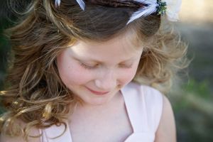 Close-up of a curly-haired girl with a floral hair accessory looking down and smiling softly in a blush pink dress.