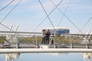 Group of people standing on a modern cable-stayed bridge overlooking calm water under a bright blue sky.