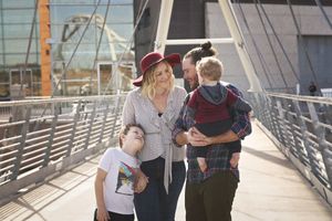 Parents and two boys walk together on a modern bridge, with the mother in a red hat and the father carrying a toddler.