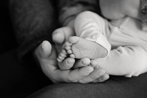 Black and white close-up of a parent's hand gently cradling a newborn baby's tiny feet.