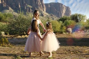 Mother and two daughters in pale pink tulle dresses holding hands while walking through a desert landscape with rocky cliffs.