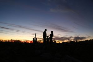 Silhouette of a family of three standing together on a rocky desert hill under a vivid purple and orange sunset sky.