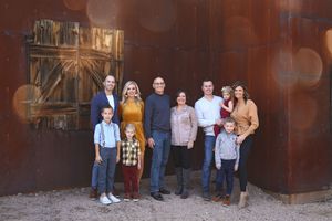 Family of ten poses outdoors in front of a rustic rusted metal wall with an old wooden barn door and warm bokeh lights.