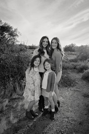 Black and white portrait of a mother and three daughters posing together outdoors among desert brush at sunset.