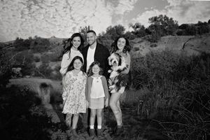 Black and white family portrait of two parents, two young girls and a fluffy dog standing in a desert landscape.