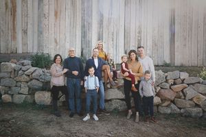 Multi-generational family poses in front of a weathered wooden barn wall and stone ledge, with parents, grandparents and children.