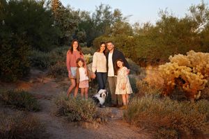 Family of four with a small dog standing among desert shrubs and cacti in warm evening light.