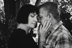 Black and white close-up of a couple touching foreheads in an intimate moment beside a tree.