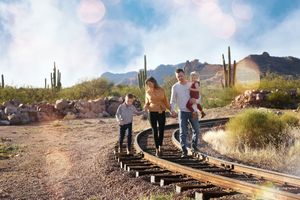 Family of four walks along old railroad tracks in the desert, with saguaro cacti and rocky mountains glowing in warm sunlight.