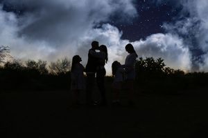 Silhouette of a family gathered together outdoors under a dramatic cloudy night sky filled with stars.
