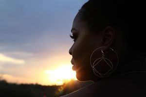 Profile silhouette of a woman wearing large hoop earrings against a glowing sunset sky.