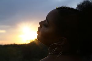 Silhouette of a woman in profile with hoop earrings tilting her face toward the glowing sunset sky.