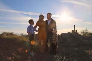 Silhouetted family of four posing together at sunset in a desert landscape with cactus and rocks under a bright sun.