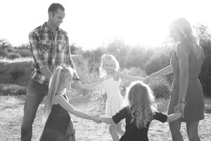 Black and white photo of a family of five holding hands in a circle outdoors, with a father, mother and three girls.