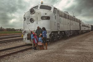 Family of five poses in front of a silver diesel locomotive numbered 97 at a rail yard under an overcast sky.
