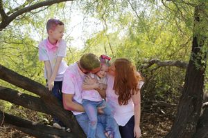 Family of four with a red-haired mother, father, young girl and boy sitting together in a tree, smiling and embracing outdoors.
