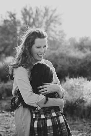 Black and white photo of a laughing mother embracing her daughter outdoors, her hair blowing in the breeze.
