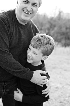 Black and white portrait of a joyful father hugging his smiling young son tightly outdoors.