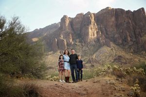 A family of four poses together on a rocky desert hill with a dramatic mountain cliff behind them.