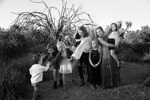 A black and white family portrait of women and children gathered playfully among desert shrubs and a bare, twisted tree.