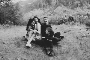 Black and white photo of a family sitting close and laughing together on the ground in a rugged desert landscape.