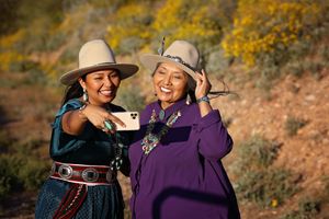 Two smiling women in wide-brimmed hats and Native American turquoise jewelry take a selfie among golden autumn foliage.