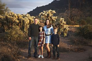 Parents and two children standing together on a desert path surrounded by cholla cactus with mountains behind them.