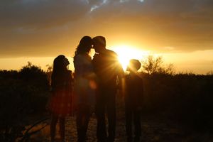 Silhouette of a family of four embracing against a glowing golden desert sunset.