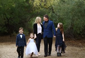 Family of five in coordinated navy outfits walking hand in hand along a tree-lined path for a portrait session.