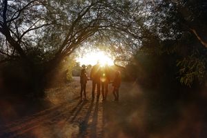 A family stands silhouetted on a wooded trail as bright golden sunset light filters through the trees.