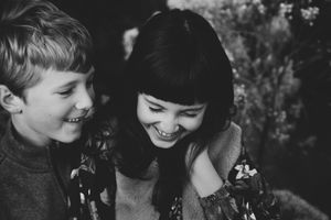 Black and white portrait of a laughing boy and girl leaning close together, sharing a joyful sibling moment.
