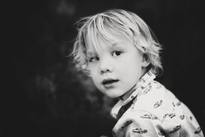 Black and white portrait of a young blond boy with tousled hair looking at the camera in a patterned collared shirt.