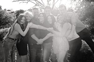 Black and white photo of a large group of smiling family members hugging closely with arms joined together outdoors.