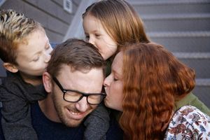 Happy family of four sharing a close, affectionate moment as the children kiss their smiling glasses-wearing father.