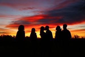 Silhouettes of a group of people gathered together against a vivid red and orange sunset sky.