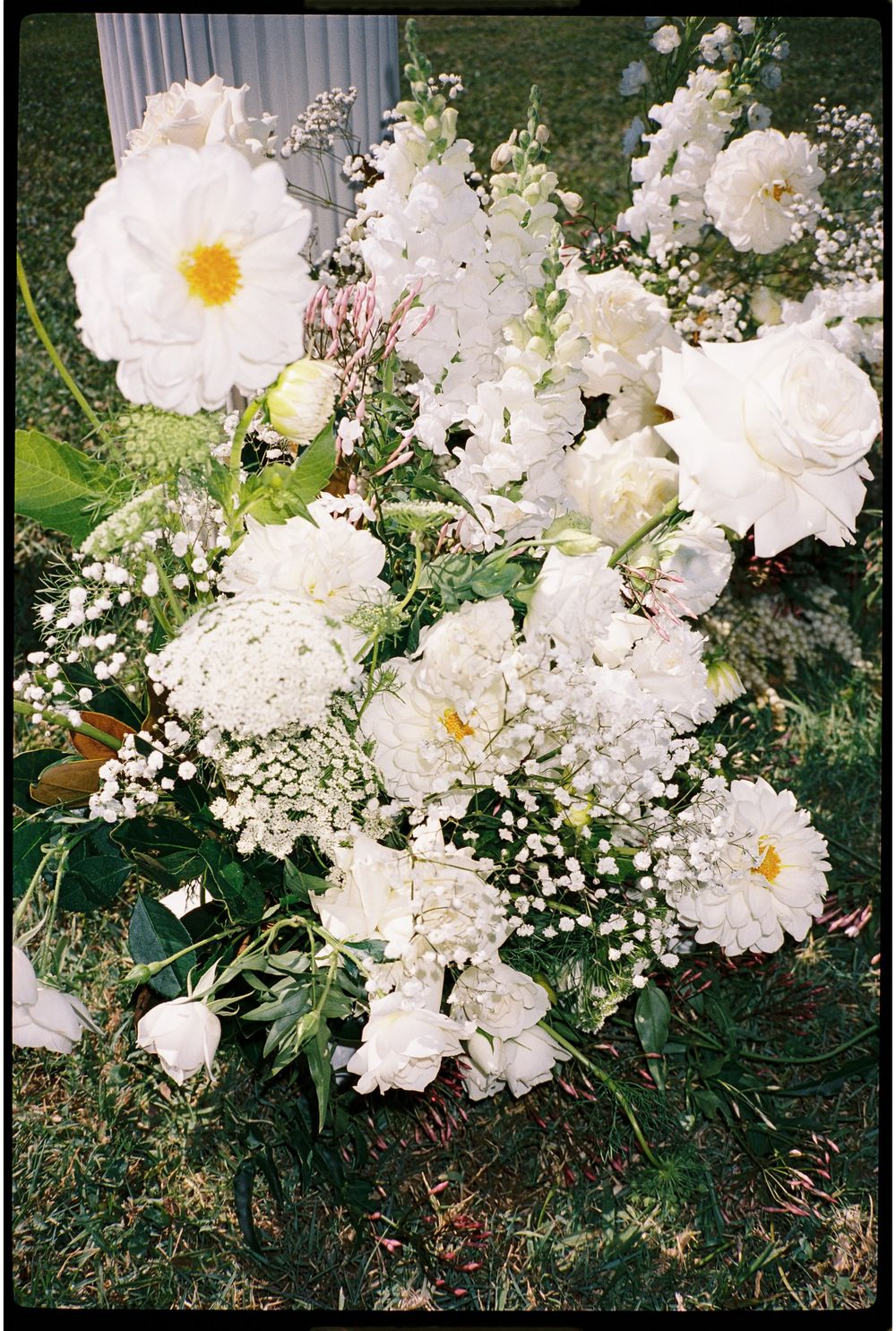 White peonies, roses, and baby's breath floral arrangement on green grass for a wedding.