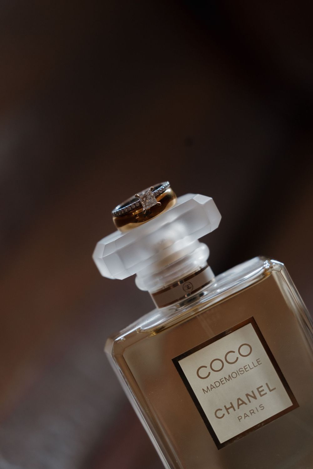 Chanel Coco Mademoiselle Paris perfume bottle with a gold ring resting on top, against a dark background.