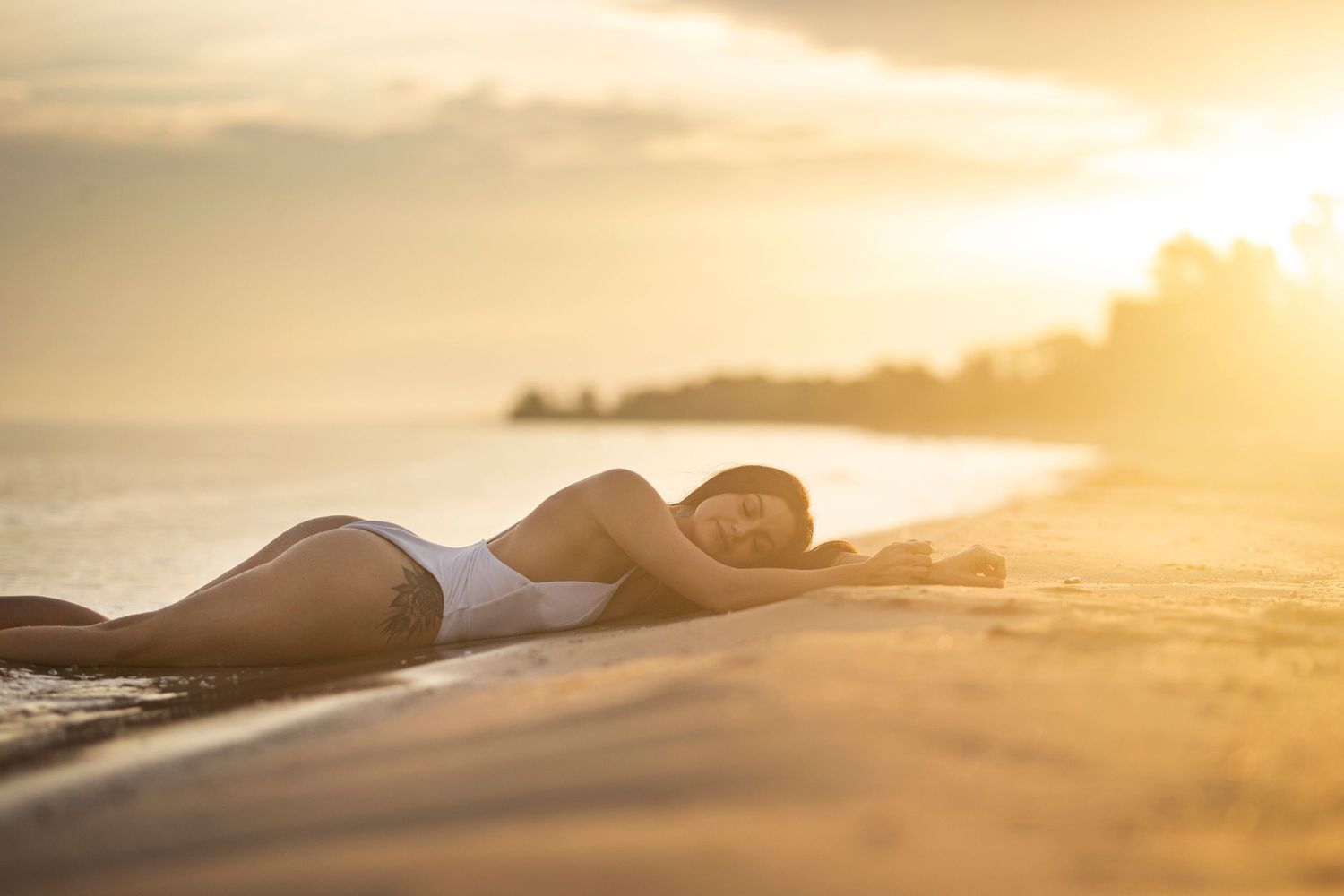 Person in white swimwear lying on beach shore during golden sunset.
