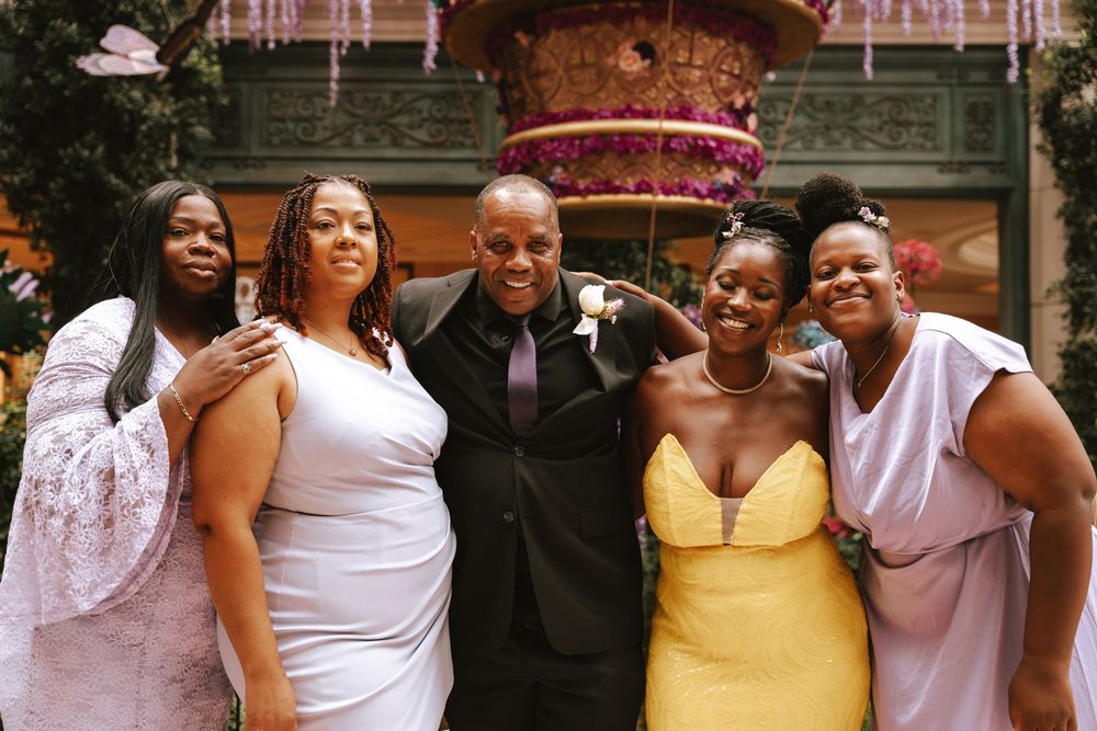 Five people pose together smiling at a formal event, wearing elegant attire including yellow and lavender dresses.
