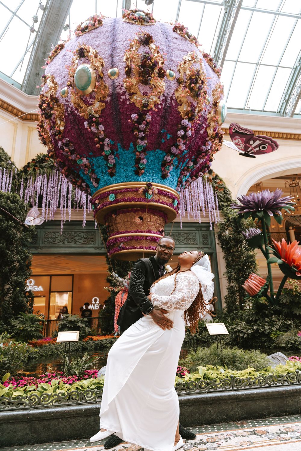 Couple sharing a romantic dip kiss under a floral hot air balloon display at Bellagio Conservatory.