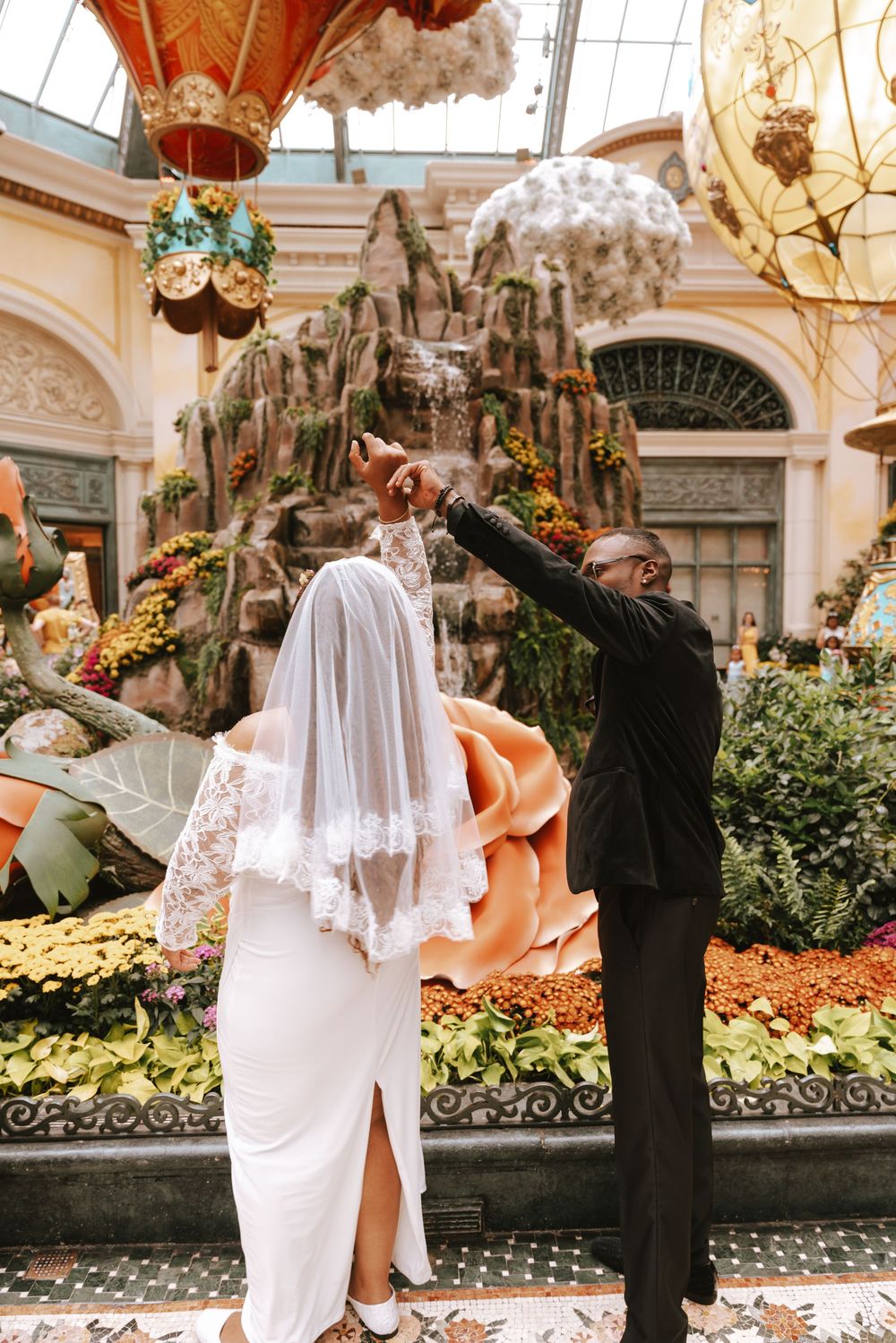 Bride and groom dancing in Bellagio conservatory, surrounded by floral displays and hot air balloon decorations.