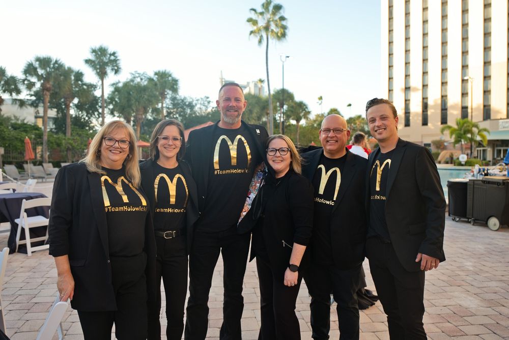 Group of seven smiling professionals wearing matching black McDonald's shirts posing outdoors at a resort event.