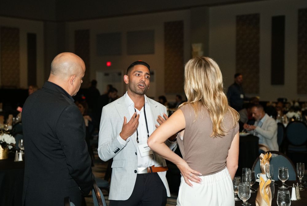 Three professionals networking at a formal banquet event, engaged in conversation near elegantly set tables.