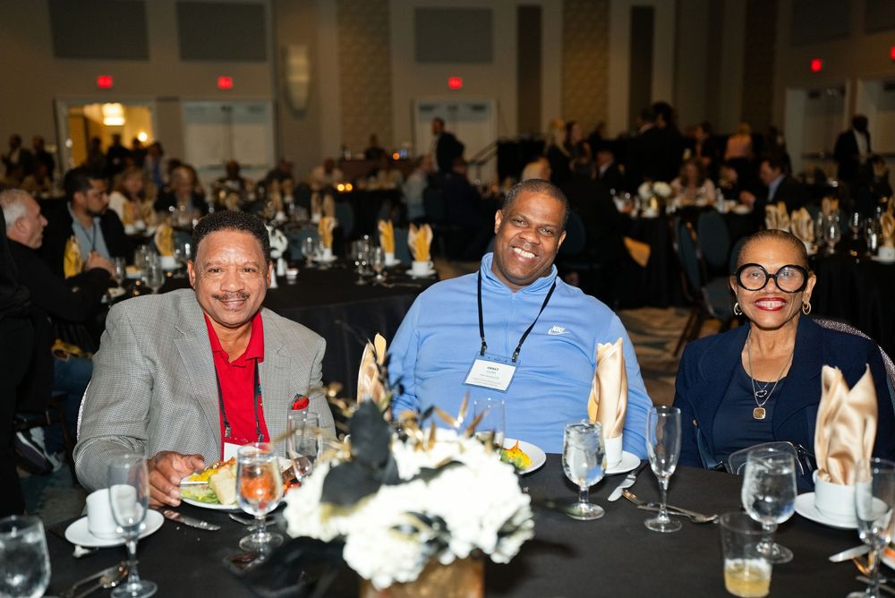 Three smiling guests seated at a banquet table during a formal gala dinner event in a large ballroom.