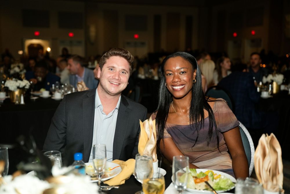A smiling man and woman pose together at a formal dinner gala event with elegant table settings.