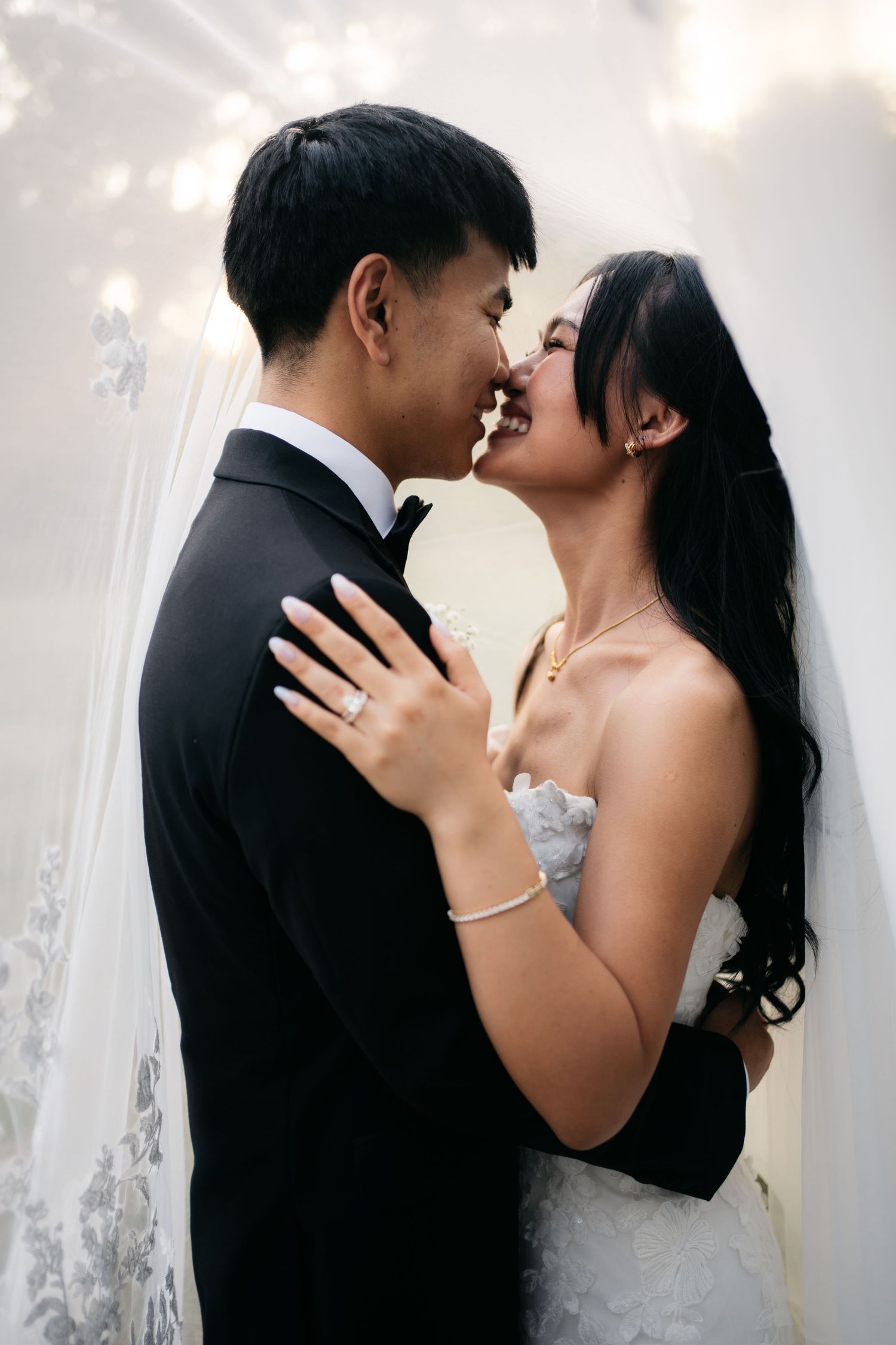Joyful bride and groom share an intimate almost-kiss moment surrounded by sparkling lights at their wedding.