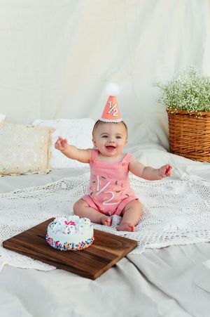 Happy baby in pink romper celebrating half birthday with cake.