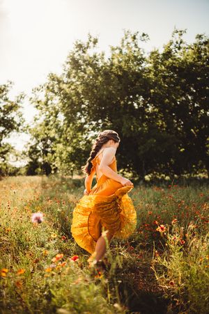 Young girl in a flowing yellow dress running through a vibrant wildflower field in golden sunlight.