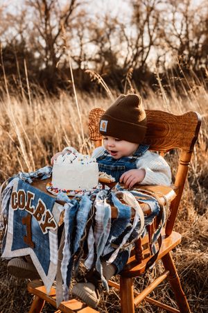 Baby boy named Colby celebrating first birthday with white cake outdoors in golden field.
