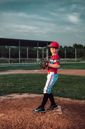 Young baseball pitcher in red uniform standing on mound with glove.